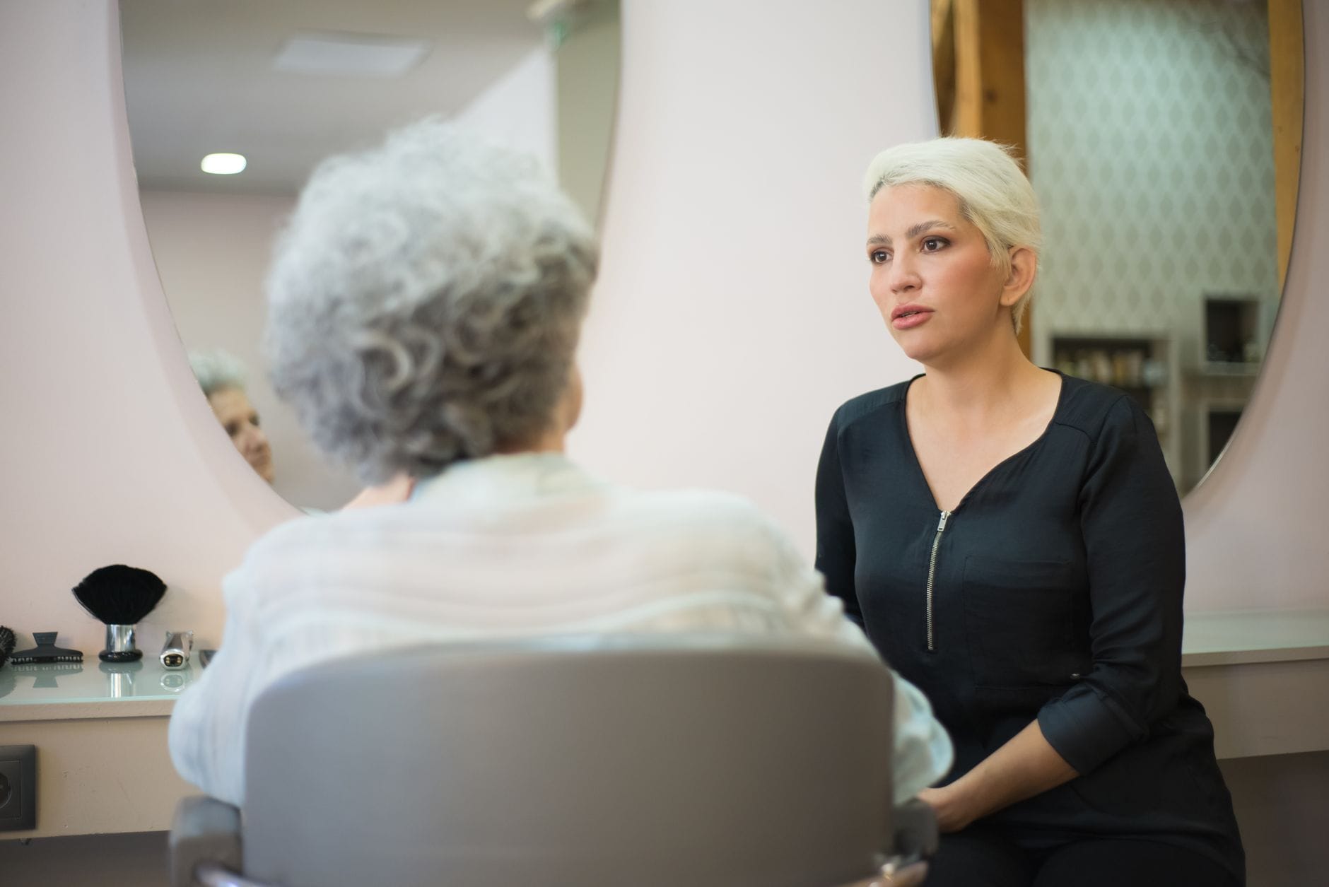 Dwie kobiety rozmawiające w salonie beauty przed lustrem